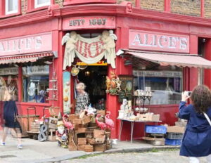 Frontage of Alice’s antique shop on Portobello Road in Notting Hill, painted bright red and spilling out onto the pavement with curios, crates and flamingo ornaments.